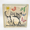 Une veilleuse en bloc de verre transparent, éclairée de l'intérieur par des guirlandes lumineuses à LED chaudes. Le verre est décoré de motifs en vinyle : un grand dessin noir stylisé de deux chats assis dos à dos, un soleil jaune en haut à gauche, un grand papillon orange en haut au centre, un colibri vert en haut à droite, un papillon bleu à droite et un petit papillon rouge en bas à droite. Le texte "Freesbee & Gypsie" est écrit en noir en bas du bloc. L'arrière-plan est un studio blanc épuré.