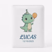 Protège-carnet de santé en cuir blanc, présenté en gros plan sur un fond blanc uni. La couverture est ornée d'une illustration de style dessin animé représentant un petit dinosaure vert portant un chapeau de fête rayé et tenant un ballon orange. En dessous de l'illustration, le prénom 'LUCAS' est écrit en lettres capitales bleu foncé, suivi de la date '12/10/2025'. Les bords du carnet sont cousus.