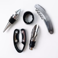Gros plan des 5 accessoires de sommelier en métal argenté et détails noirs : un limonadier, un bouchon hermétique, un stop-goutte, un collier de bouteille et un découpe-capsule.