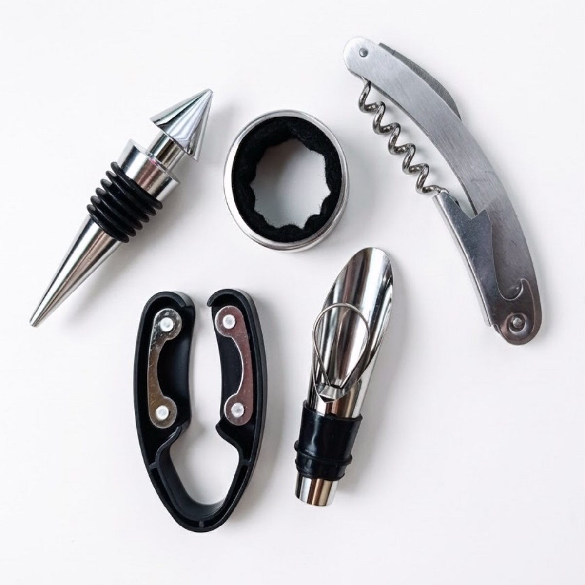 Gros plan des 5 accessoires de sommelier en métal argenté et détails noirs : un limonadier, un bouchon hermétique, un stop-goutte, un collier de bouteille et un découpe-capsule.